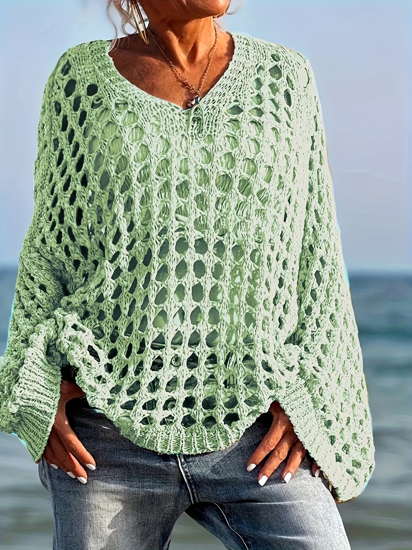 Person wearing a green lace sweater by the ocean