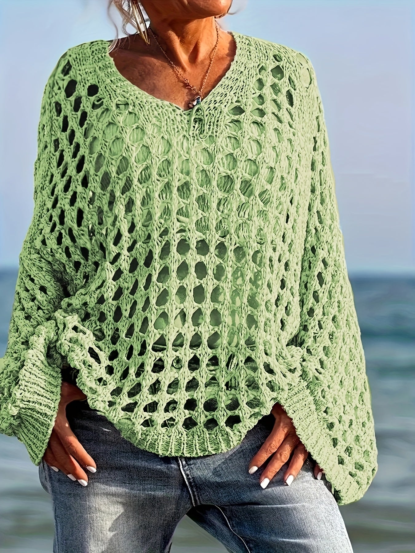 Person wearing a green lace sweater by the ocean