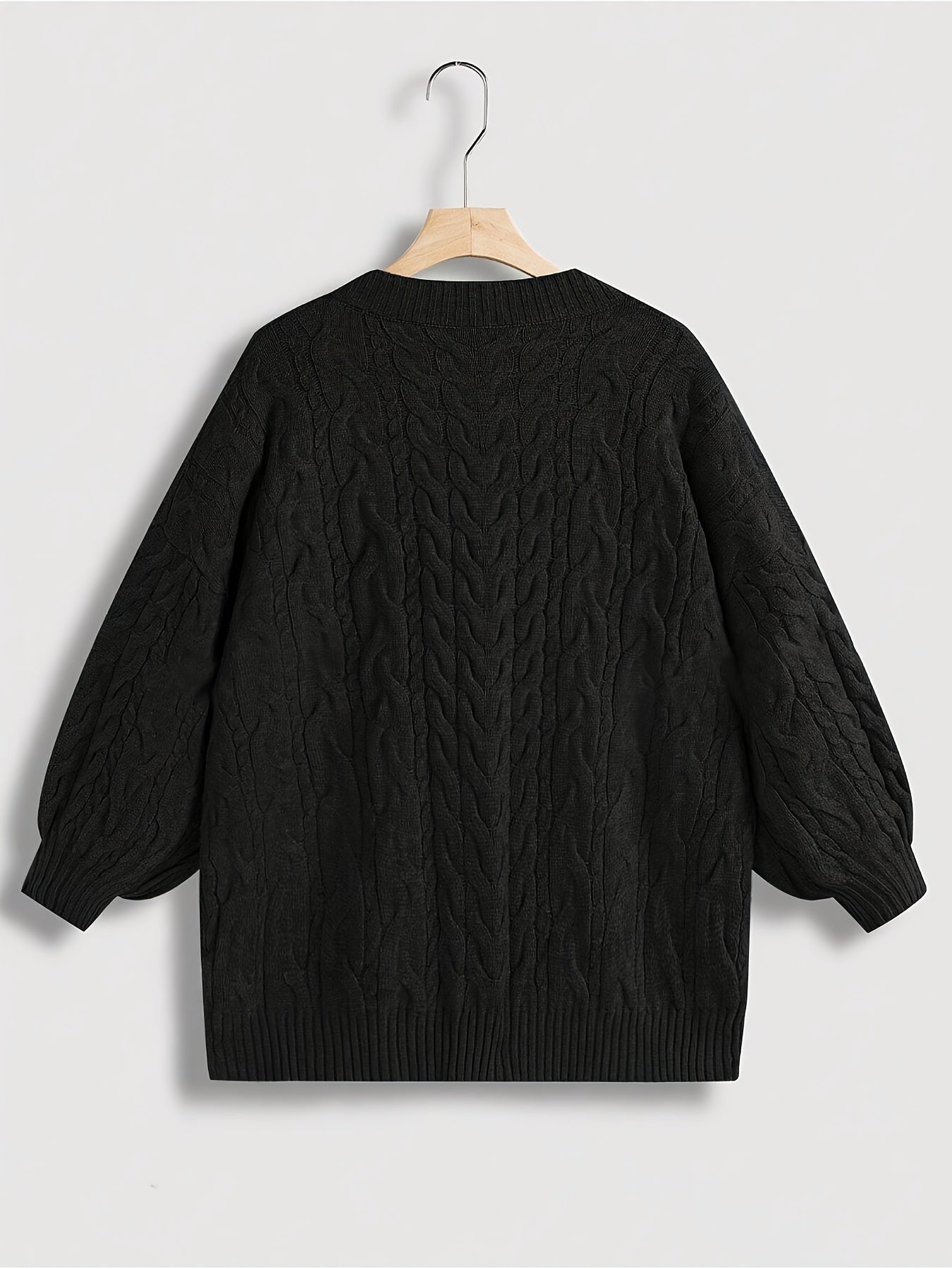 Black cable knit sweater on a hanger against a light gray background