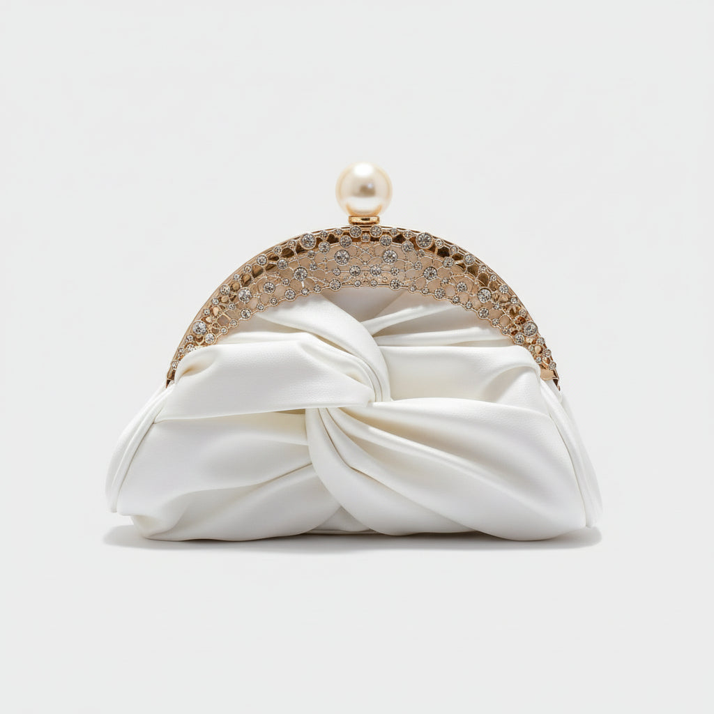 White clutch with decorative gold and pearl handle held by a hand against a neutral background
