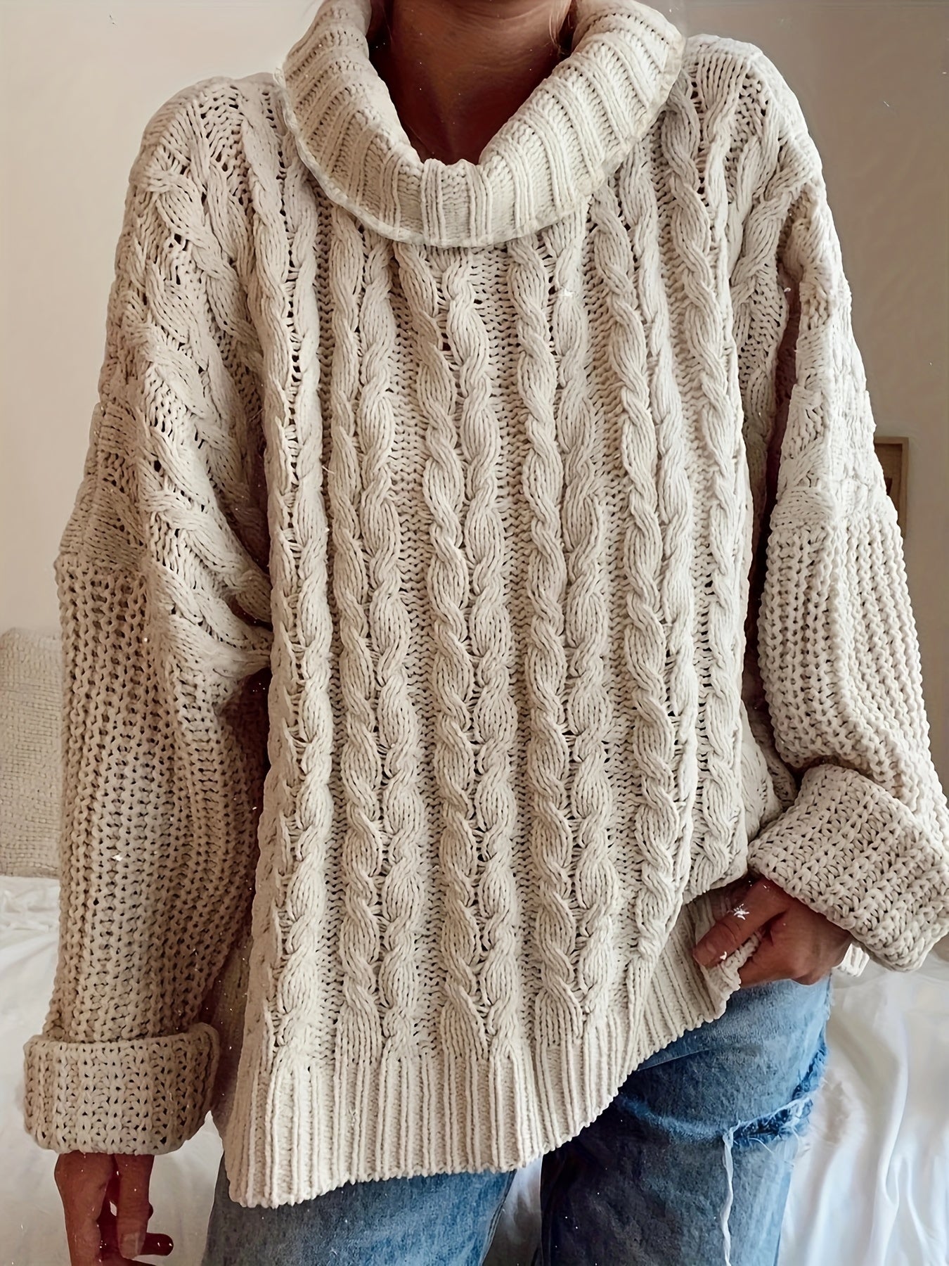 Person wearing a beige cable knit sweater with rolled-up sleeves.