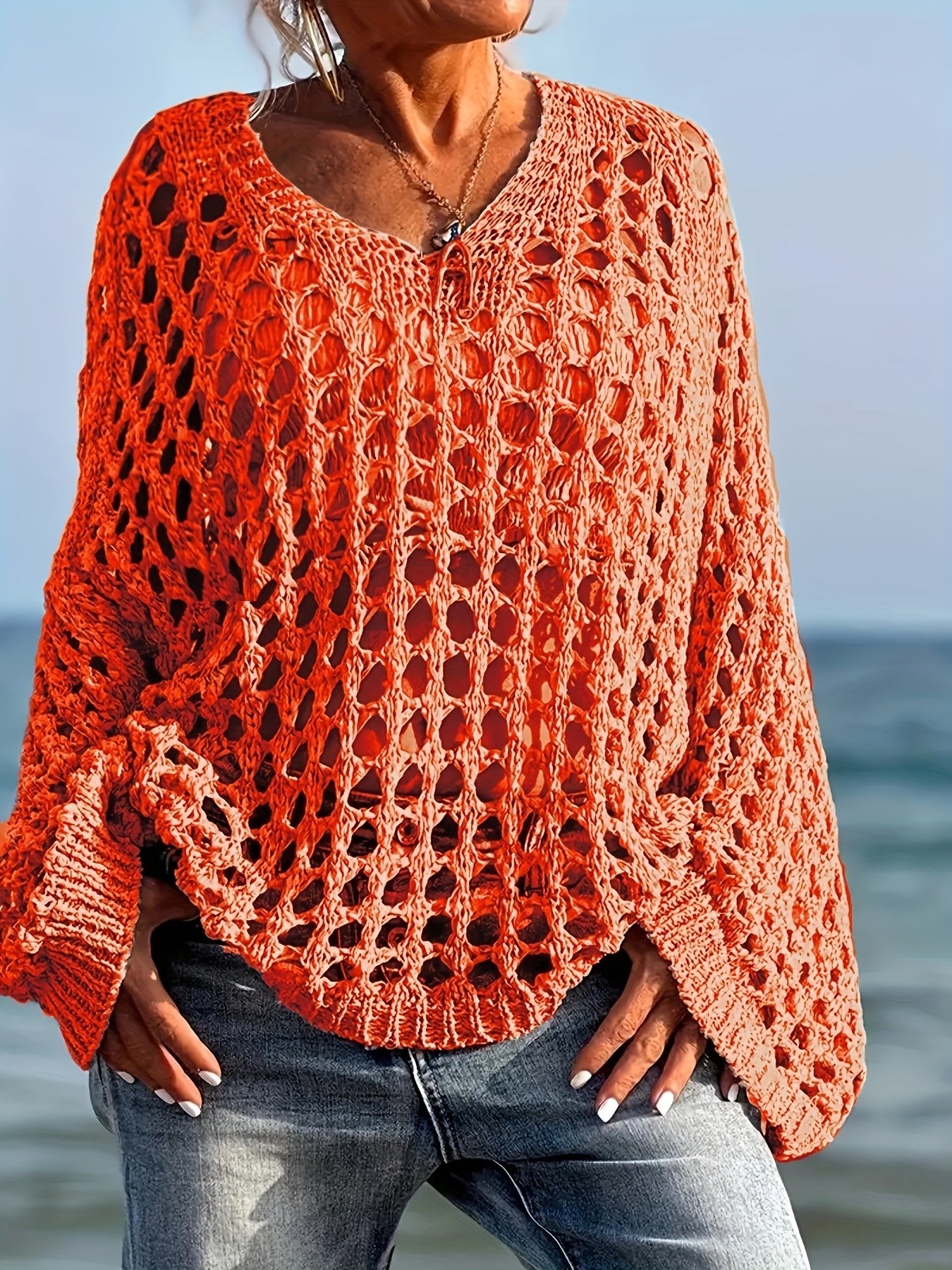 Person wearing a bright orange crochet sweater by the ocean