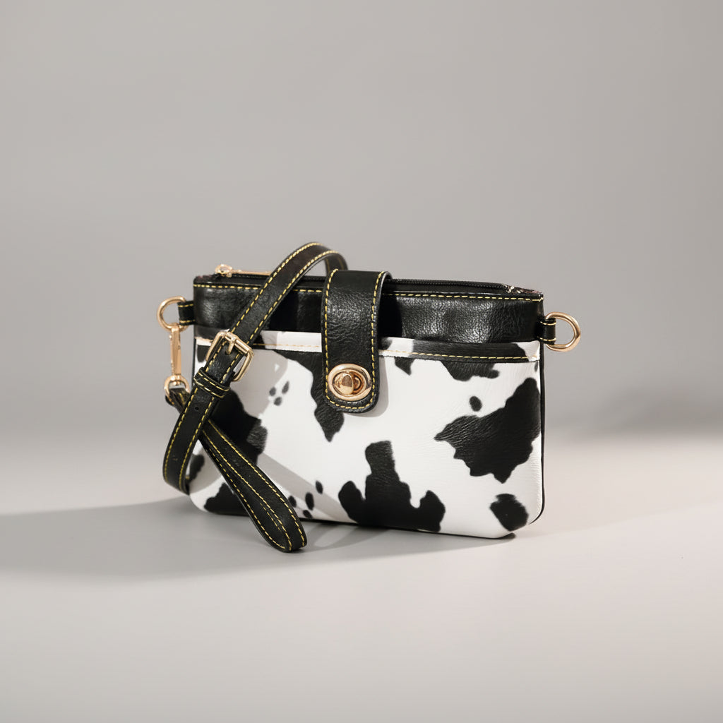 Black and white cow print handbag with gold accents on a gray background