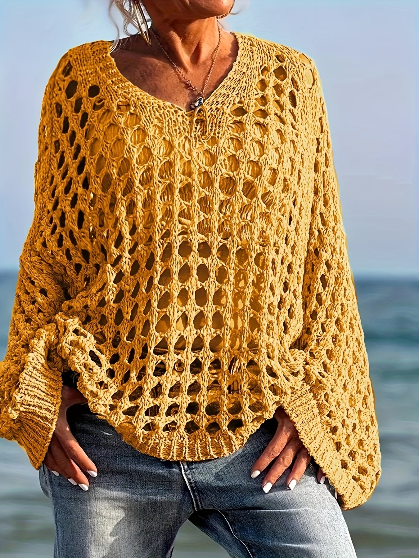 Person wearing a yellow crochet sweater by the ocean