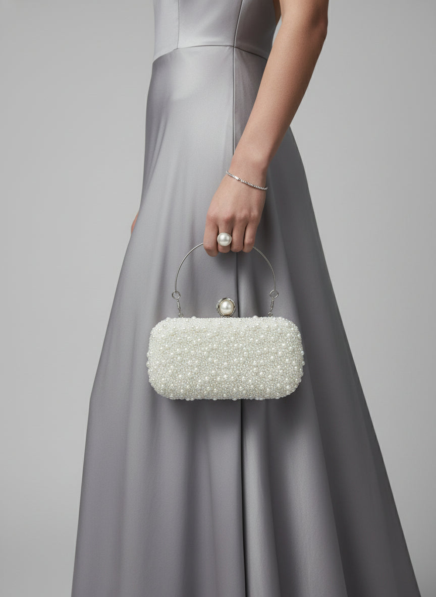 White beaded handbag held by a hand with red nail polish against a light background