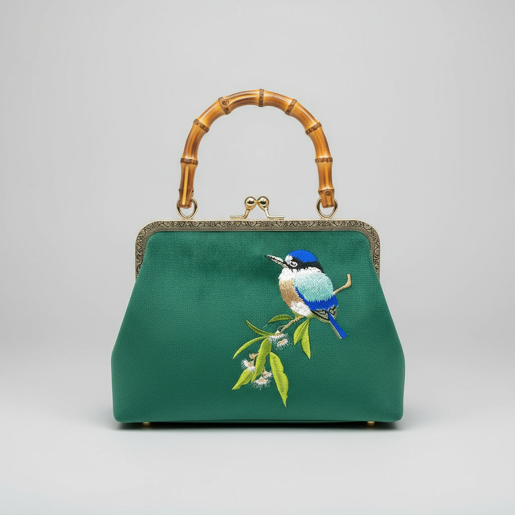 Green handbag with bird embroidery and bamboo handle on a light surface with a blurred background