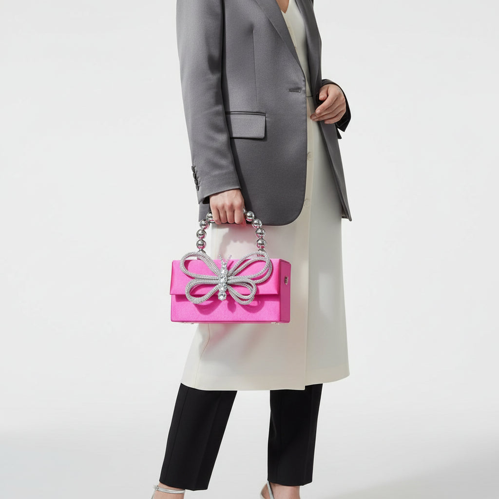 Pink handbag with a silver butterfly embellishment on a textured surface