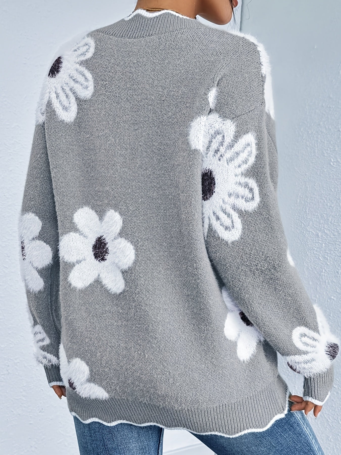 Gray sweater with white floral patterns worn by a person against a light gray background
