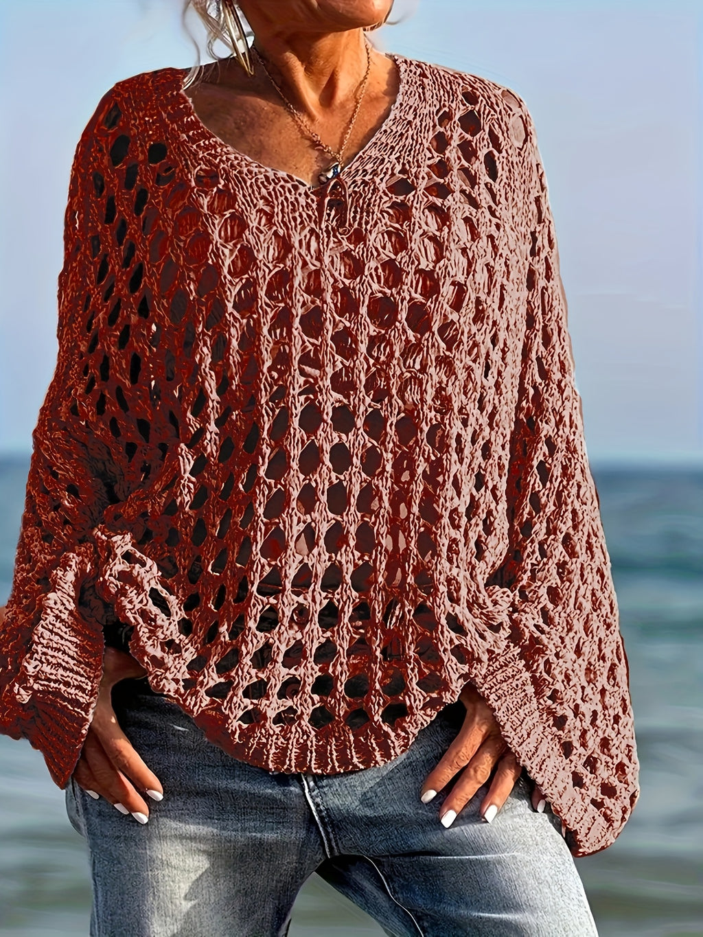 Person wearing a brown crochet sweater by the ocean