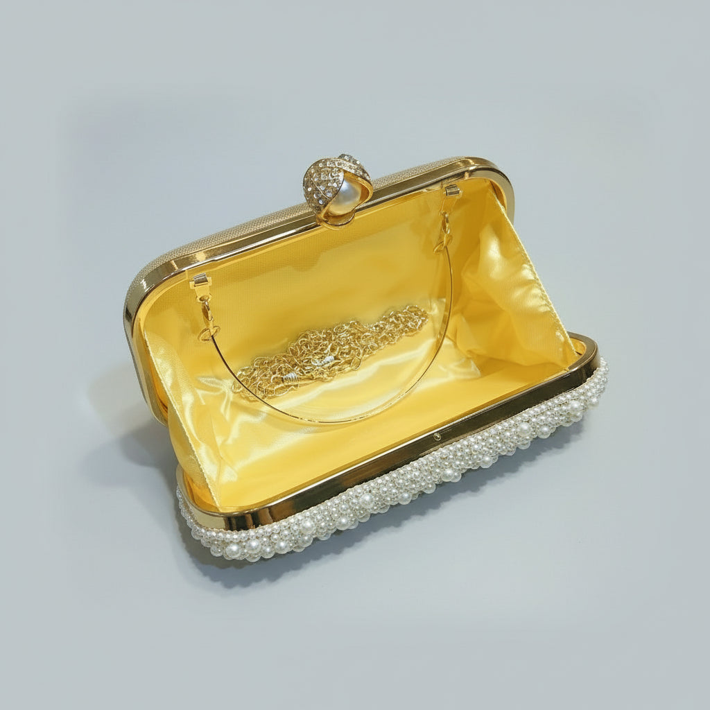 Gold clutch bag with pearl accents held by a hand against a light background