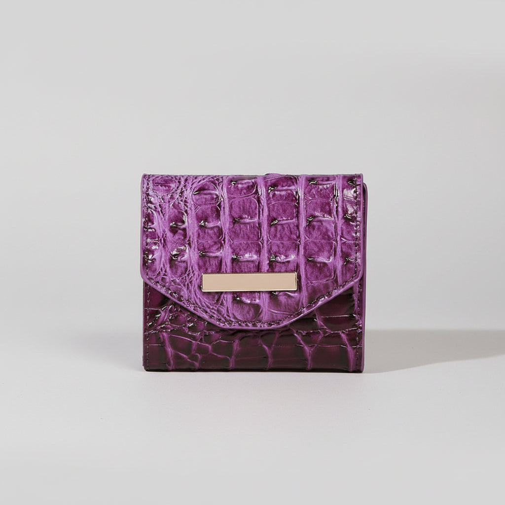 Purple textured wallet with a gold accent on a light surface, with a wooden box and fabric swatch in the background.