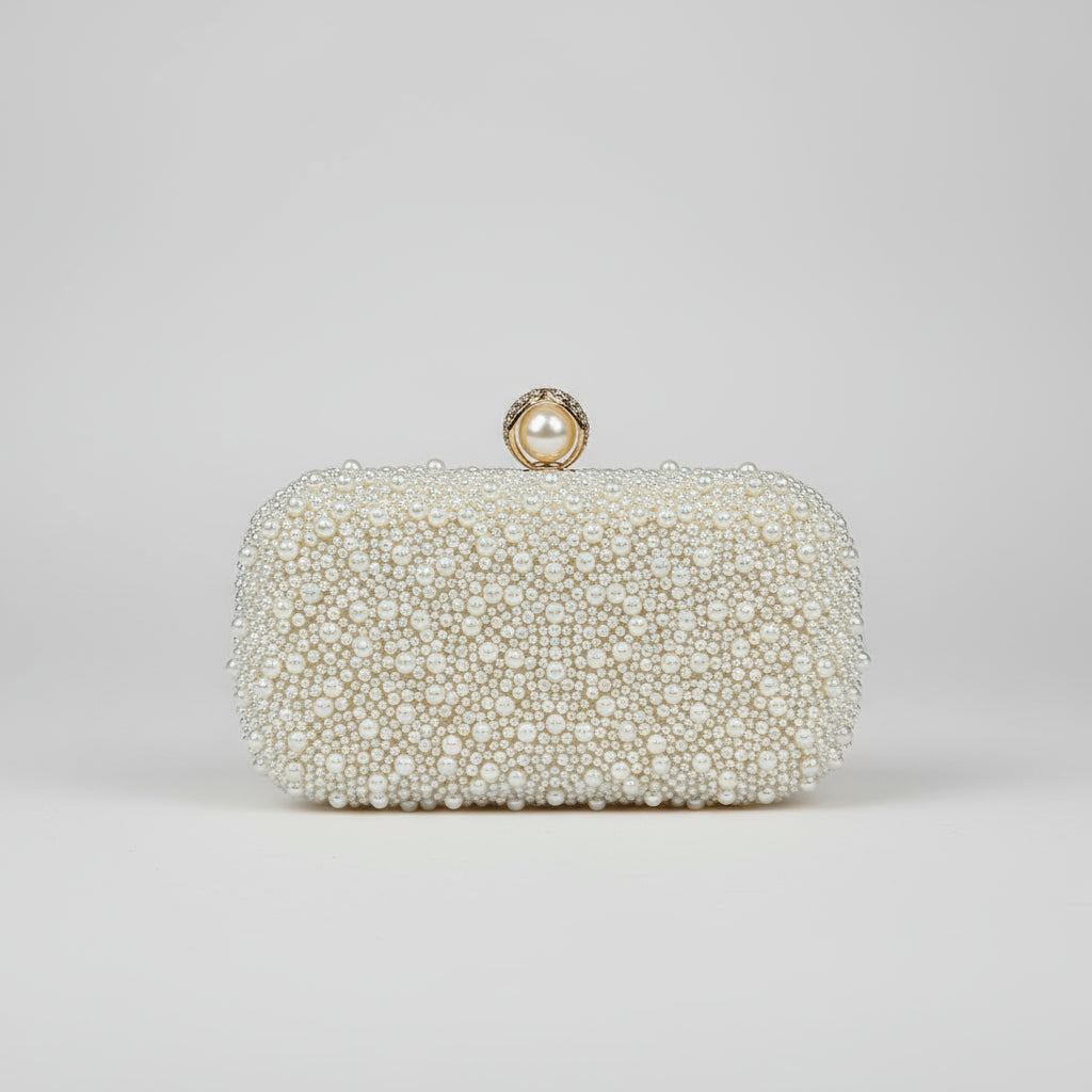 Pearl-handled clutch held by a hand with red nail polish against a blurred background