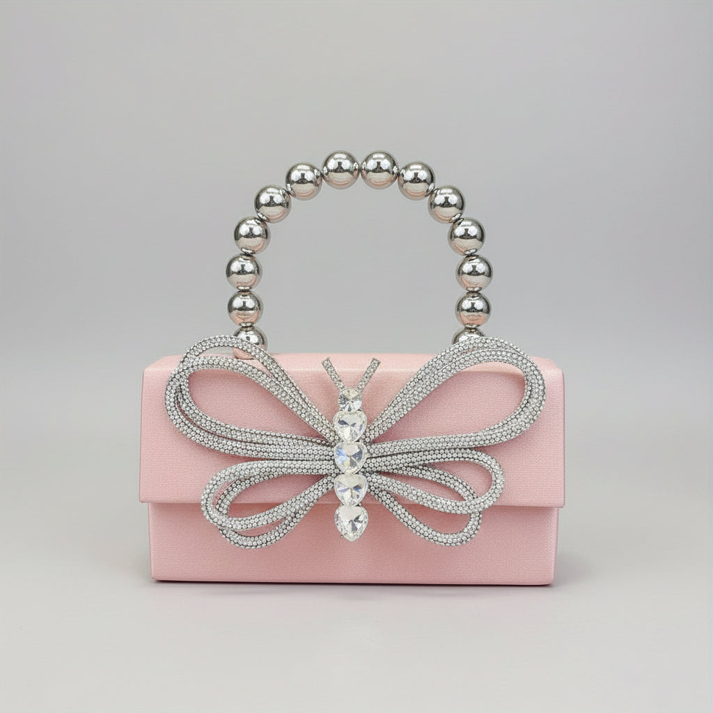 Pink clutch with butterfly design and beaded handle held by a hand.