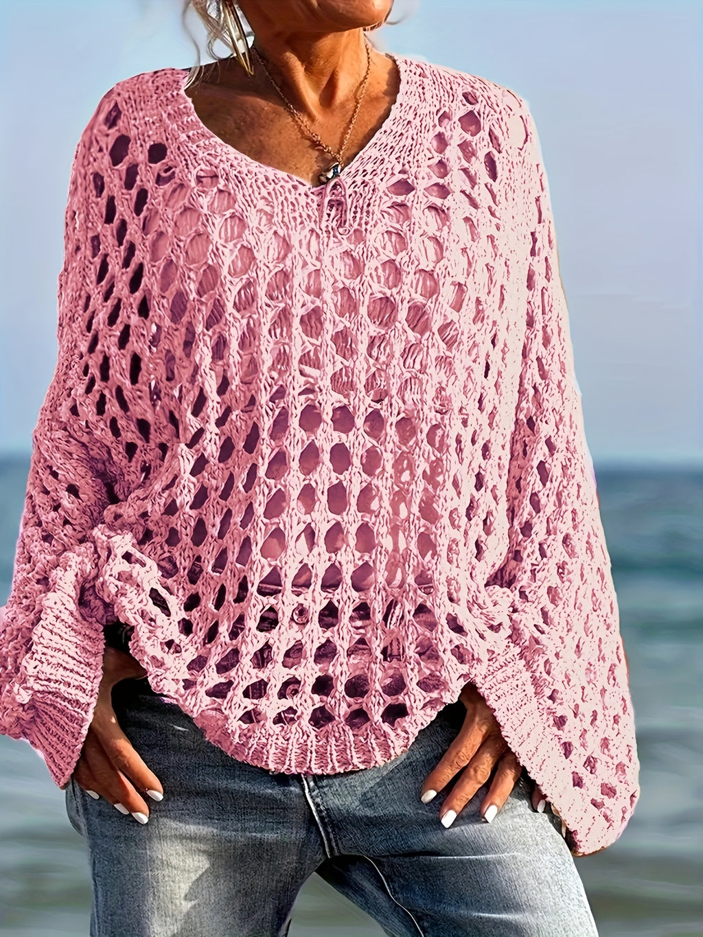 Person wearing a pink crochet sweater by the ocean