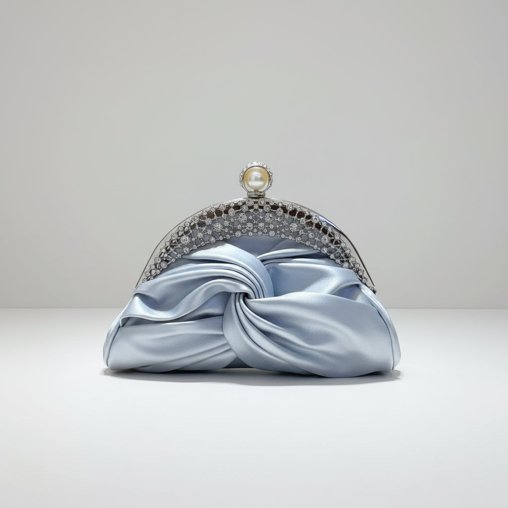 Hand holding a light blue satin clutch with a decorative silver and pearl embellished handle against a neutral background.