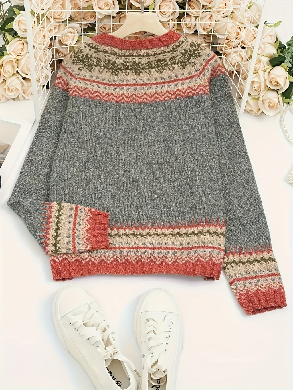 Gray sweater with patterned sleeves and hem on a white surface with flowers in the background