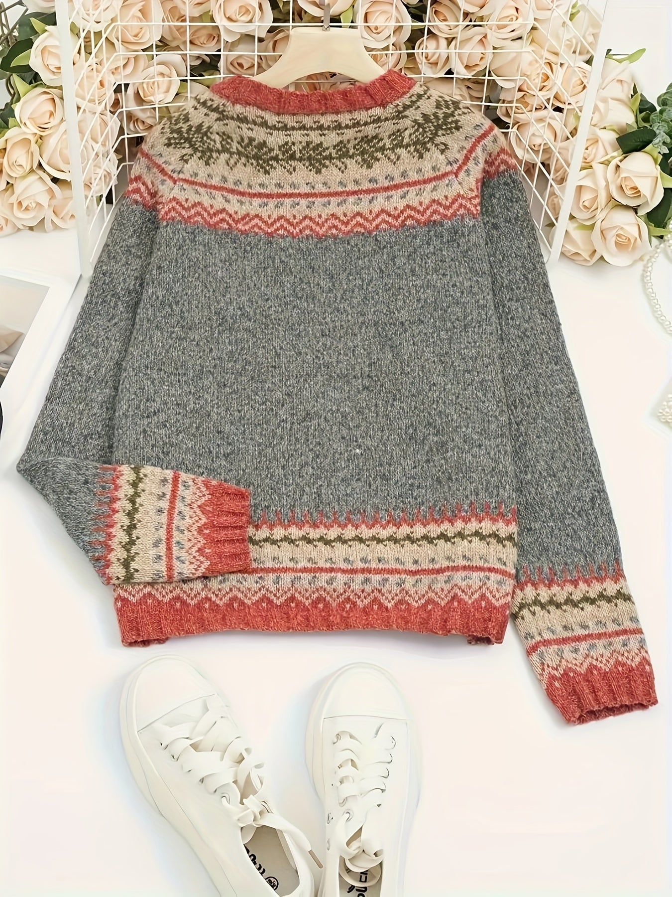 Gray sweater with patterned sleeves and hem on a white surface with flowers in the background