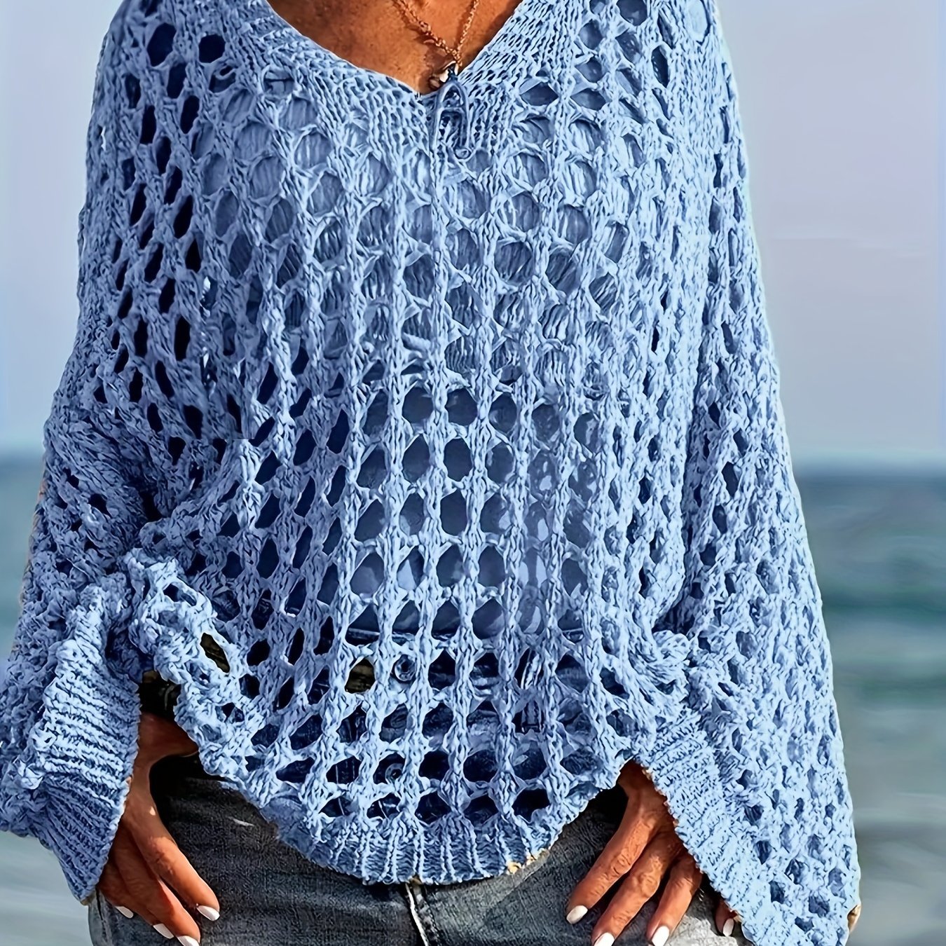 Person wearing a blue crochet sweater by the ocean
