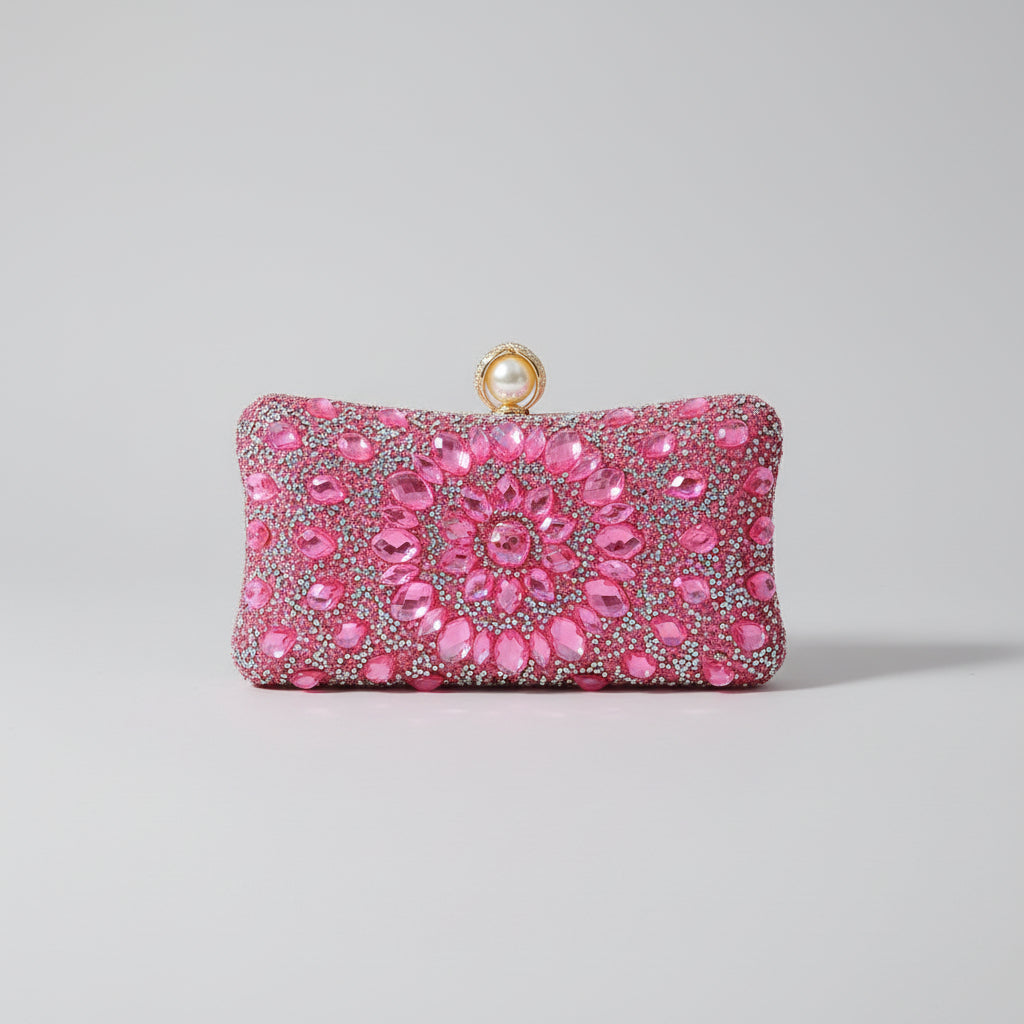 Pink clutch bag with gemstones held by a hand against a neutral background