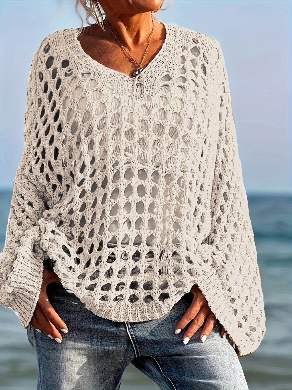 Person wearing a beige crochet sweater by the ocean