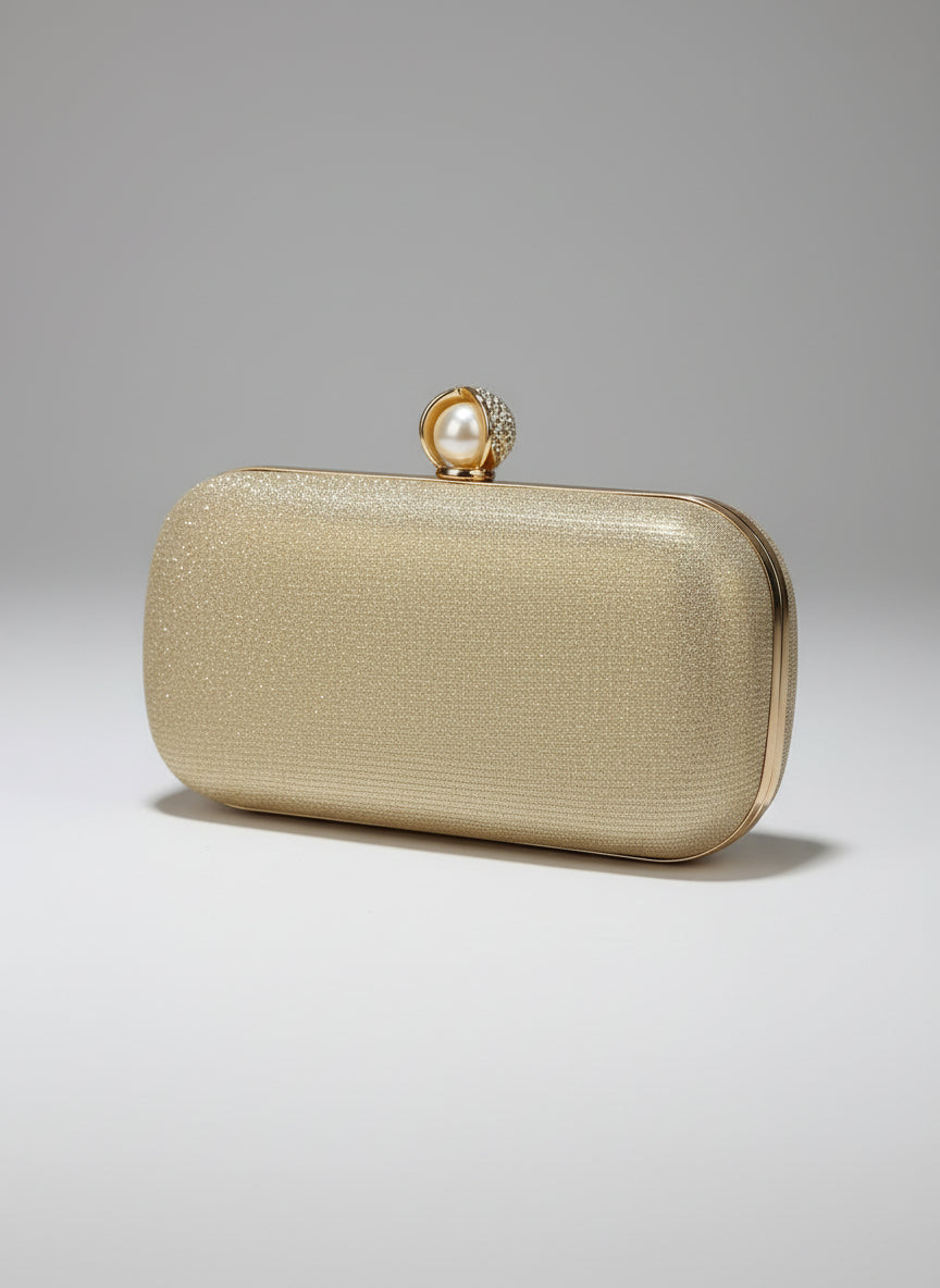 Gold clutch with pearl clasp held by a hand against a blurred decorative background