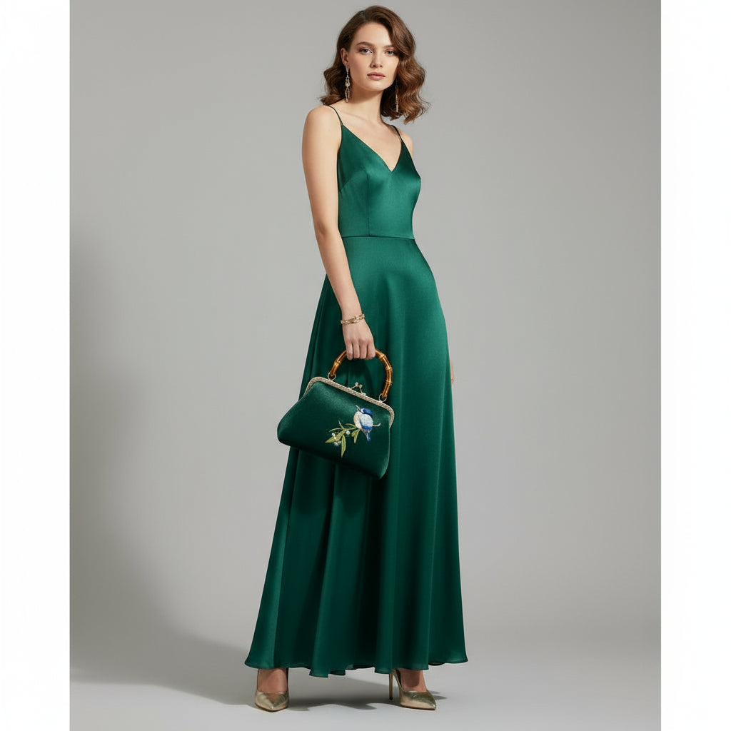 Green clutch bag with embroidered bird and bamboo handle on a white background