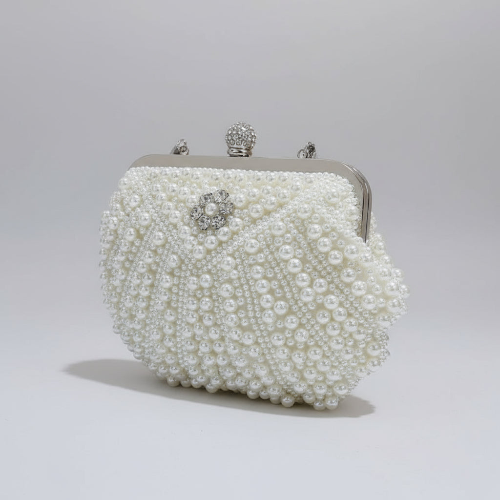 Pearl-handled clutch bag held by a hand against a neutral background