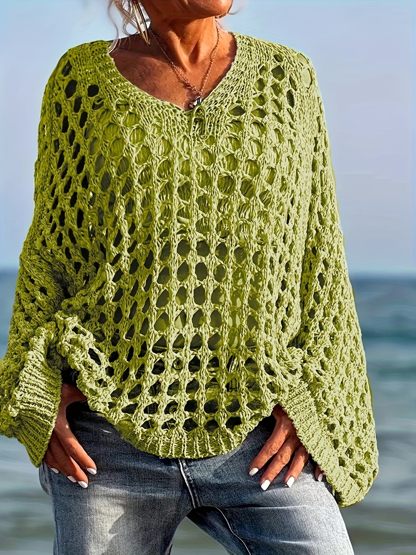 Person wearing a green lace sweater by the ocean
