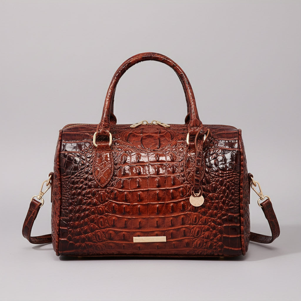 Brown crocodile-patterned handbag on a wooden surface with a dark background