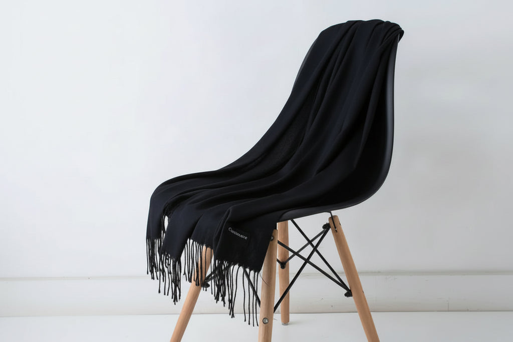 Black throw blanket draped over a white chair with wooden legs on a light background