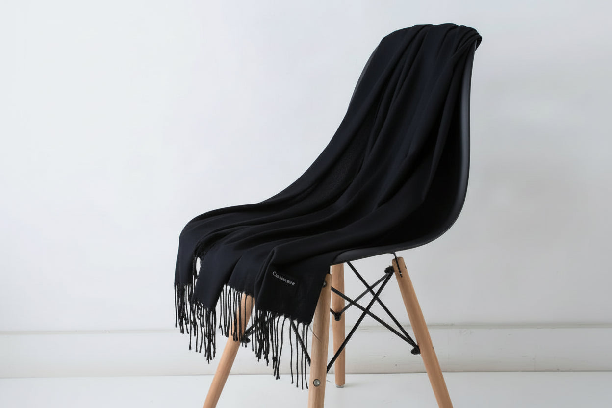 Black throw blanket draped over a white chair with wooden legs on a light background