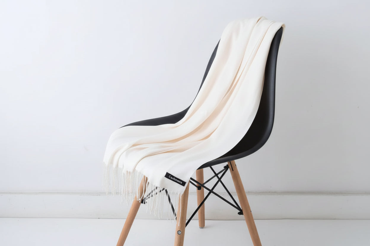 Beige throw blanket draped over a white chair with a plant in the background