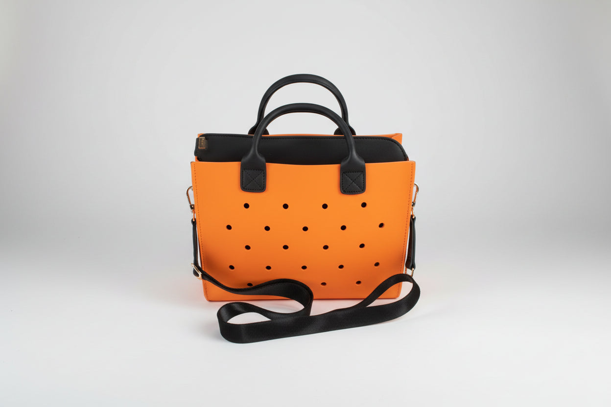 Orange polka dot handbag with black handles and strap on a light gray background