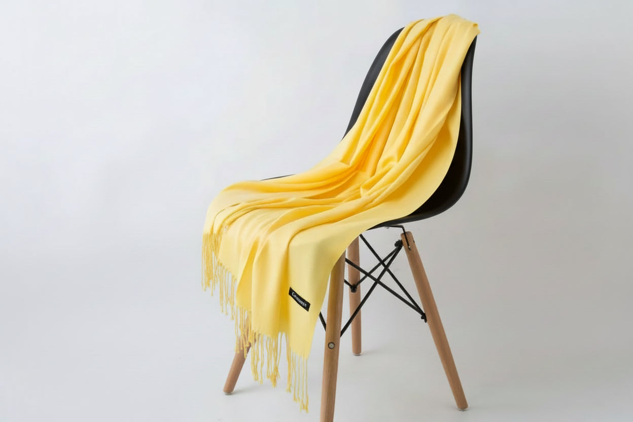 Yellow throw blanket draped over a white chair with a plant in the background