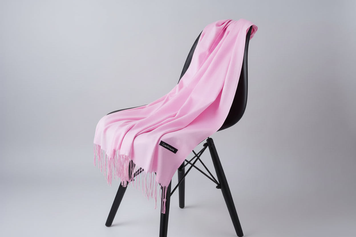 Pink scarf with tassels draped over a chair against a white background
