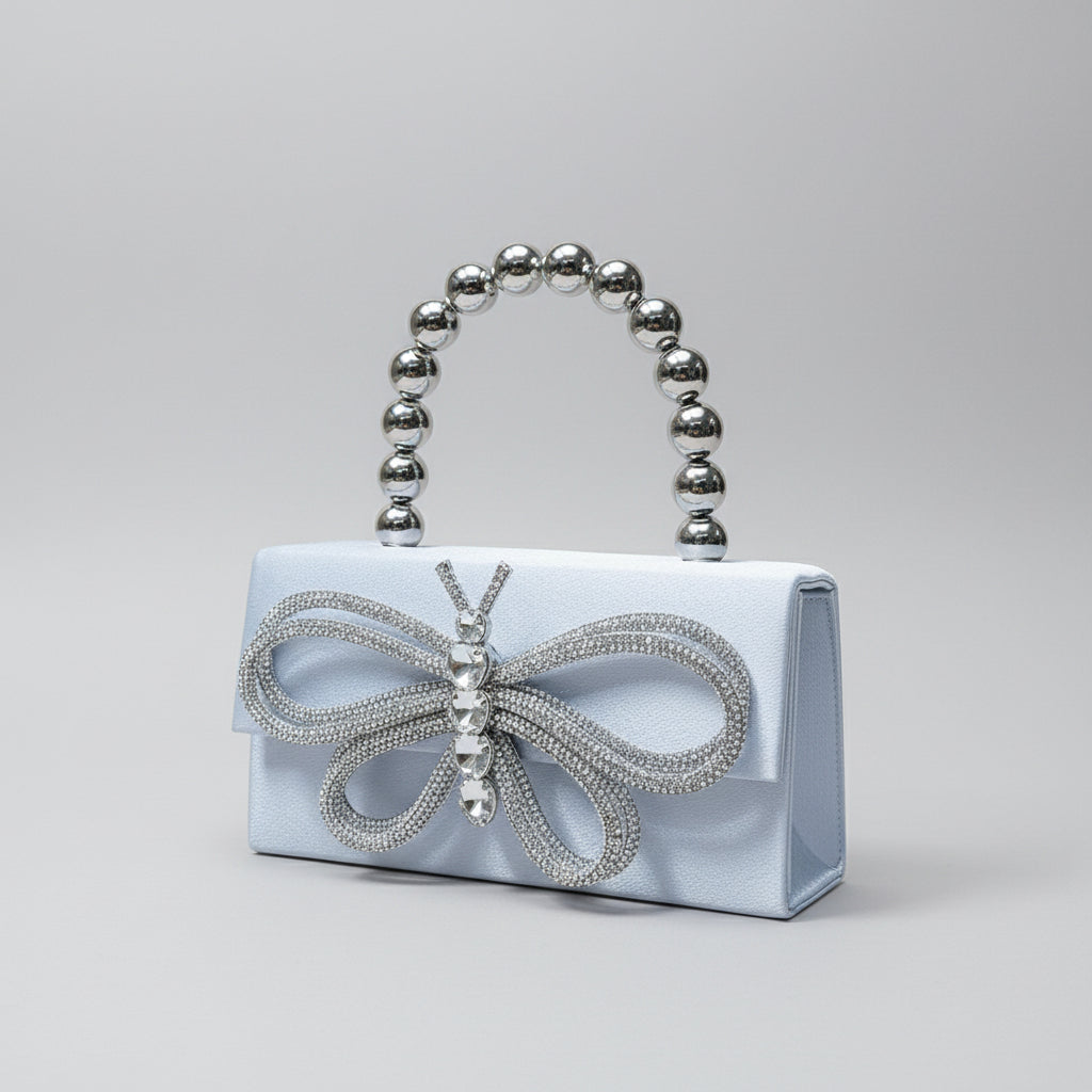 Silver clutch bag with butterfly design and beaded handle on a textured surface