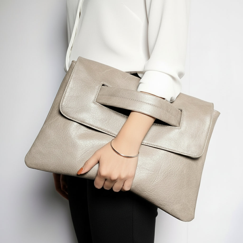 Beige clutch bag held by a person wearing a green outfit on a light gray background