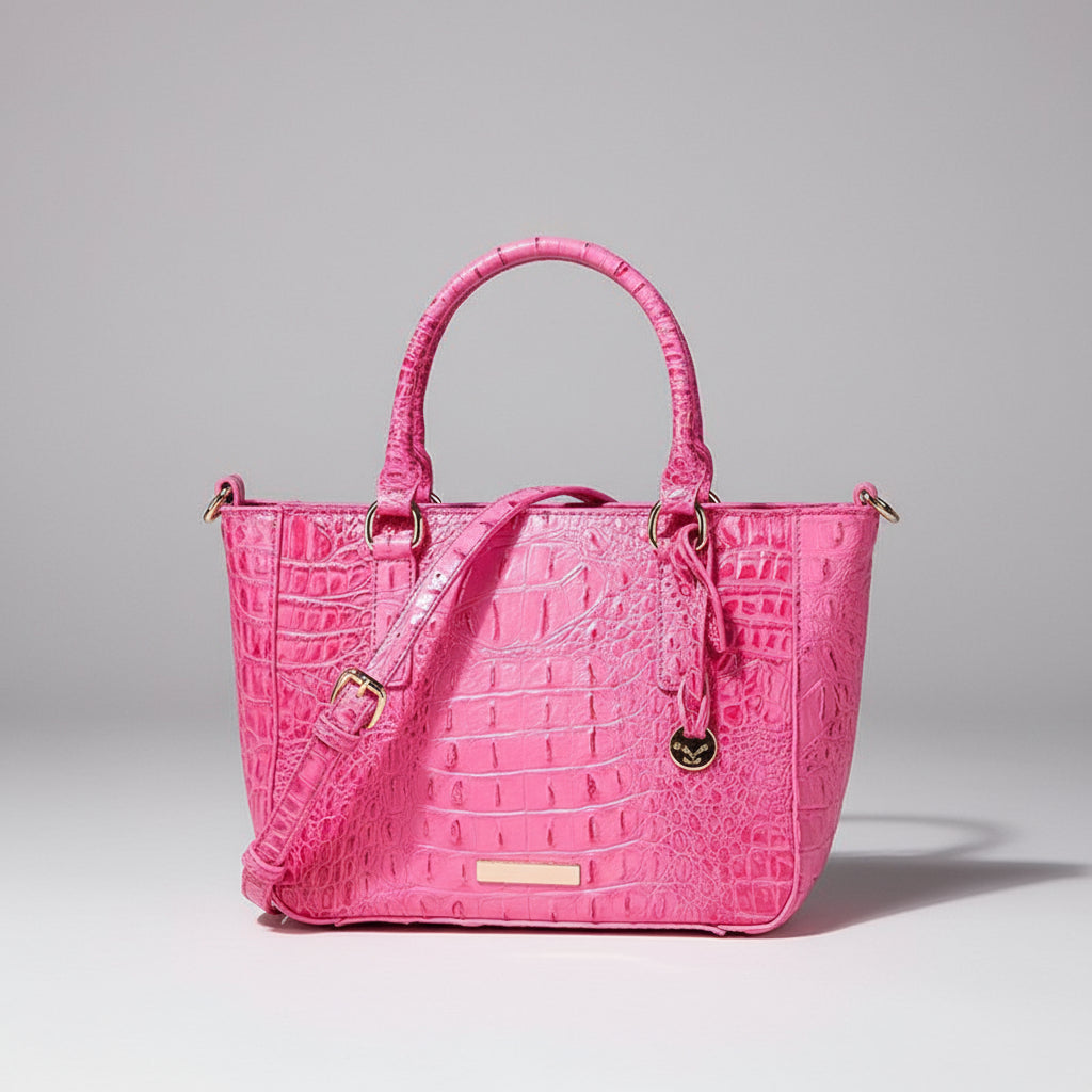 Pink crocodile-patterned handbag with gold accents on a dark background