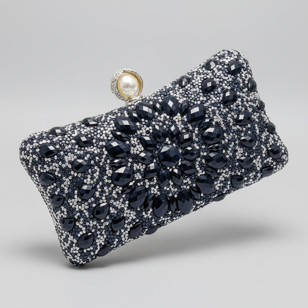 Black and silver beaded clutch held by a hand with red nail polish against a neutral background