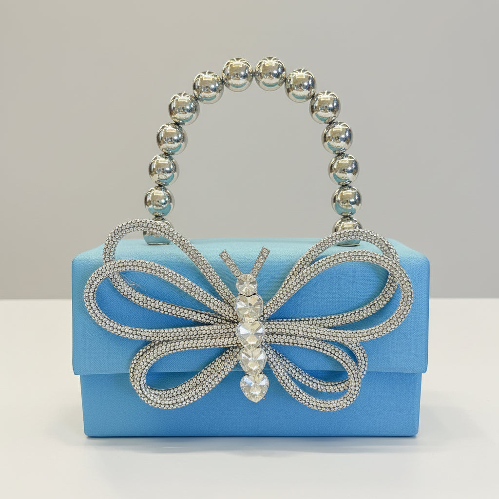 Blue handbag with a decorative butterfly and beaded handle held by a hand.