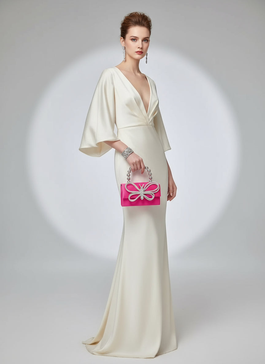 Pink clutch bag with butterfly design and beaded handle held by a person.