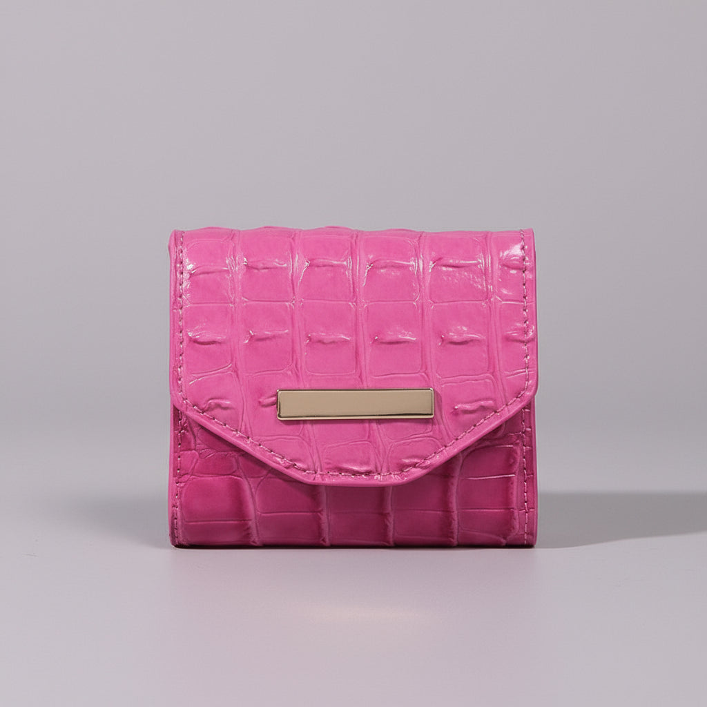Pink crocodile-patterned wallet with a gold accent on a textured surface.