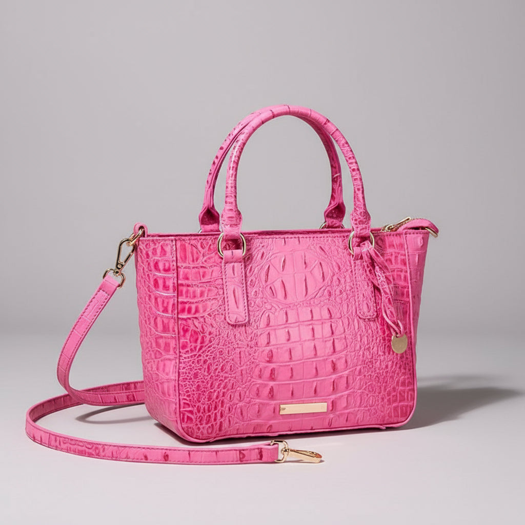 Pink crocodile-patterned handbag with a strap on a light surface.