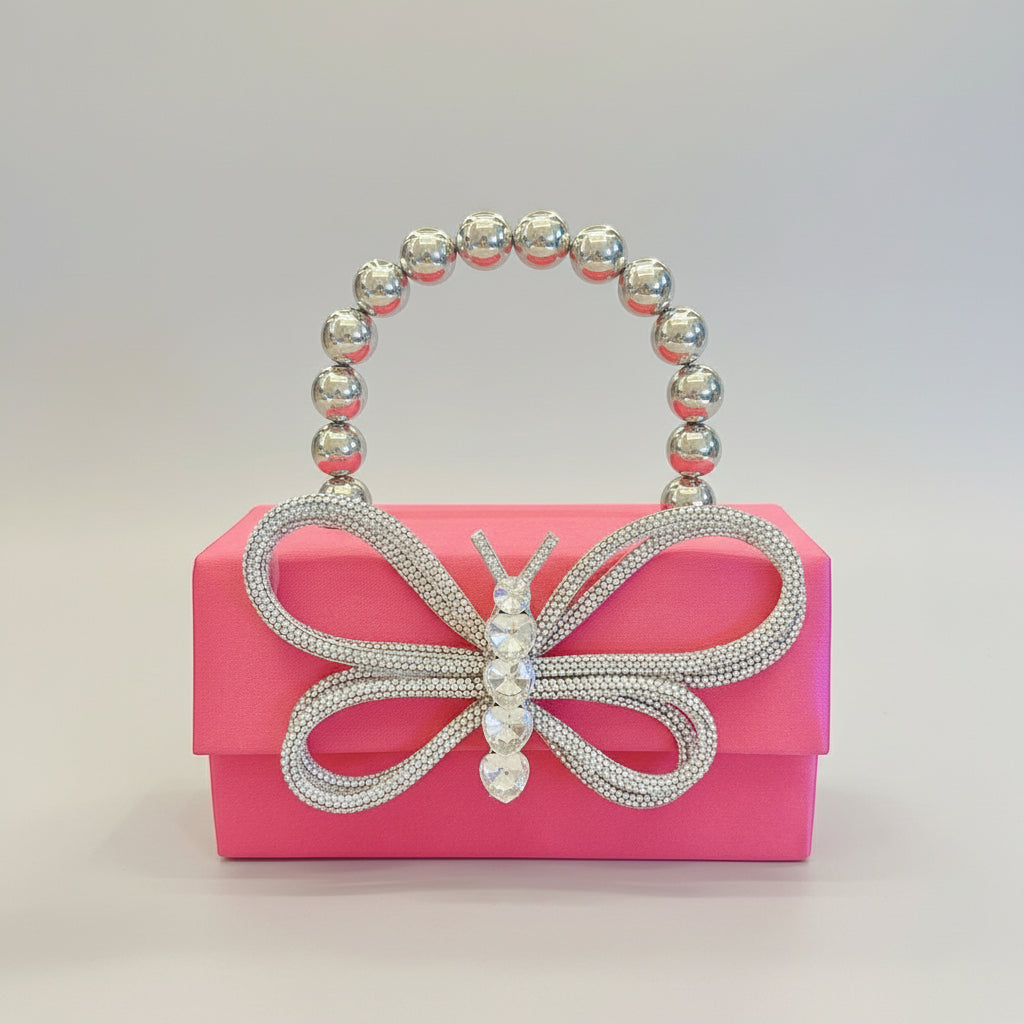 Pink clutch with butterfly design and beaded handle held by a hand against a white background