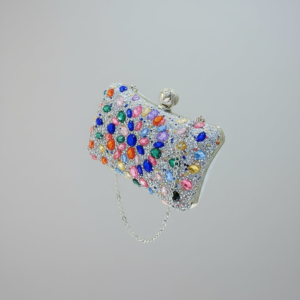 Hand holding a colorful, gemstone-encrusted clutch against a neutral background