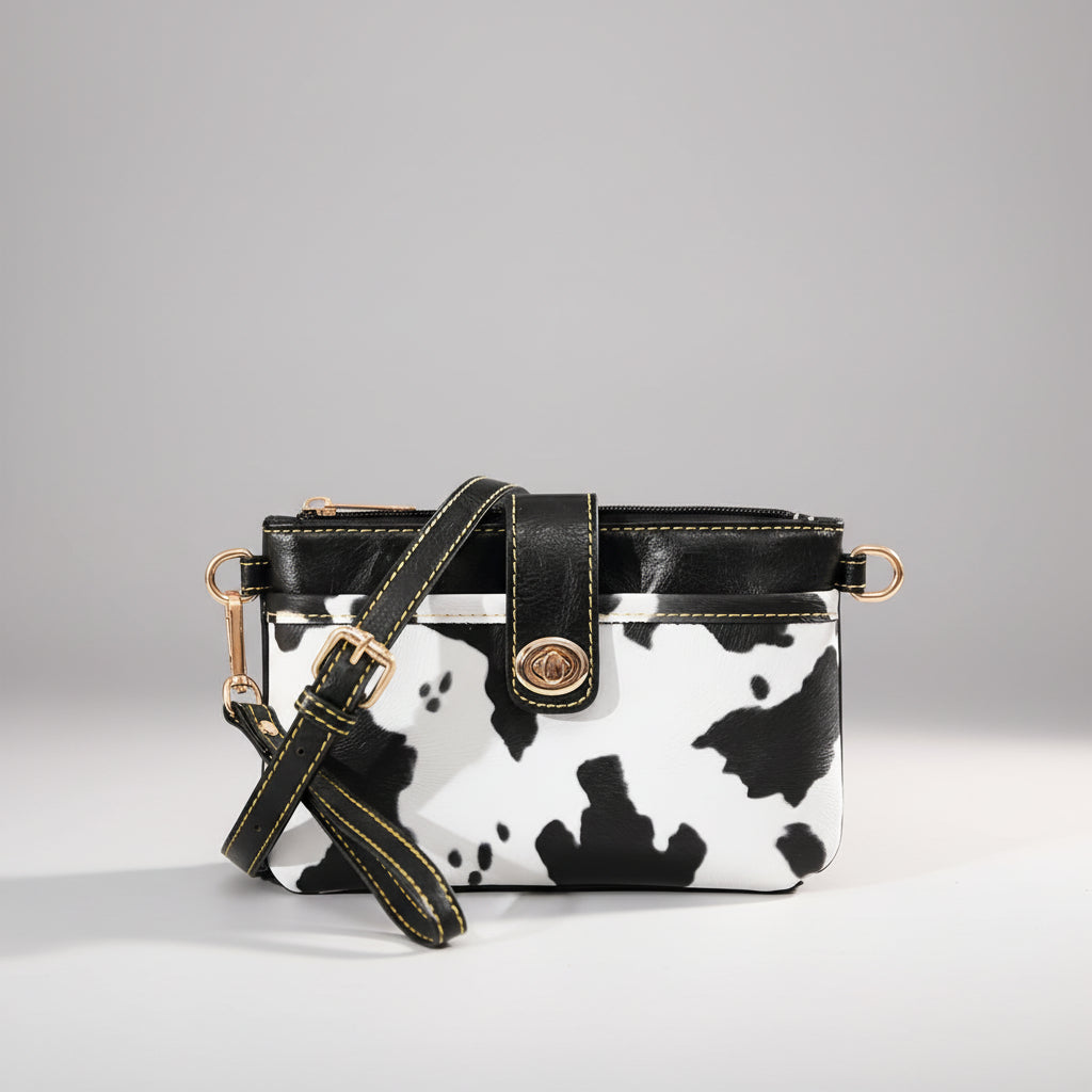 Small handbag with cow print design on a textured surface with a wooden chest in the background.