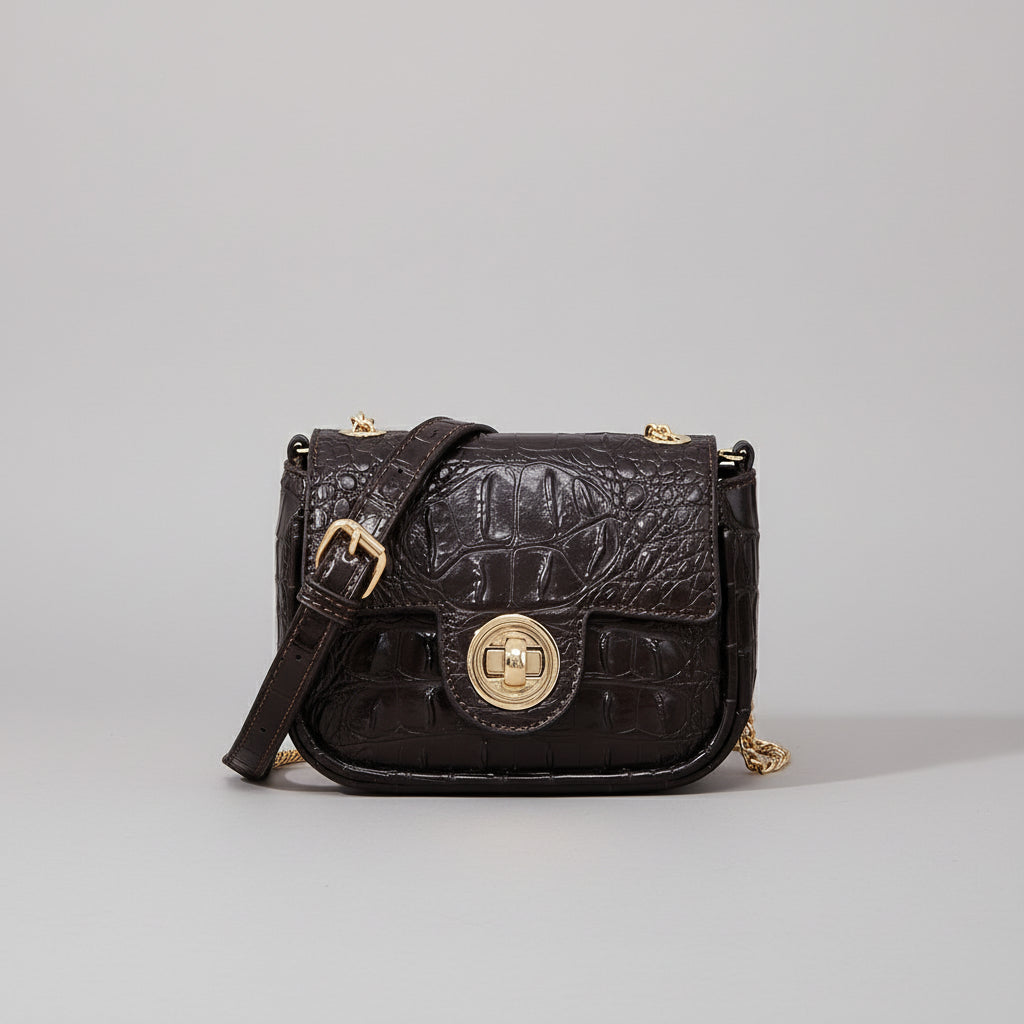 Black leather handbag with gold clasp on a wooden surface with random cut fabric pattern.